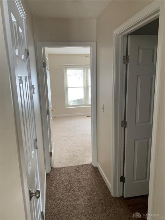 hallway featuring baseboards and dark colored carpet