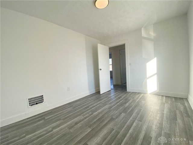 spare room with dark wood-style floors, visible vents, and baseboards