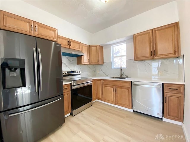 kitchen with light wood finished floors, stainless steel appliances, light countertops, a sink, and under cabinet range hood