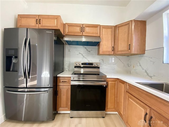 kitchen featuring stainless steel appliances, light countertops, backsplash, brown cabinetry, and extractor fan