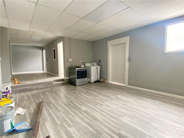 below grade area with light wood-style flooring, a drop ceiling, washer and clothes dryer, and baseboards