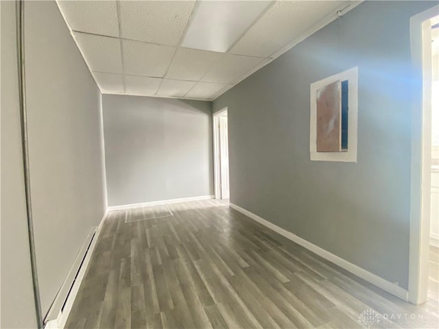 empty room with a paneled ceiling, a baseboard radiator, baseboards, and wood finished floors