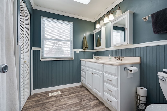 full bathroom featuring double vanity, wainscoting, crown molding, and wood finished floors