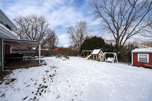 yard covered in snow with fence, a carport, and a playground