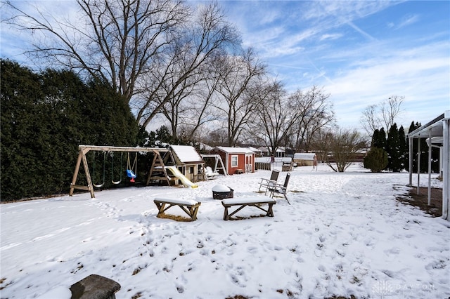 yard layered in snow featuring an outbuilding, a playground, and a shed