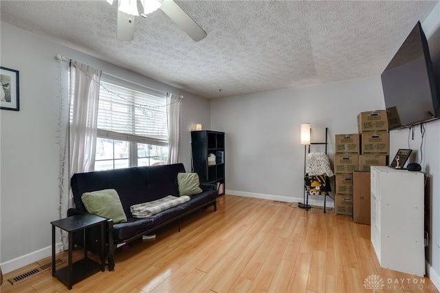 living area featuring visible vents, baseboards, light wood-style floors, a textured ceiling, and a ceiling fan