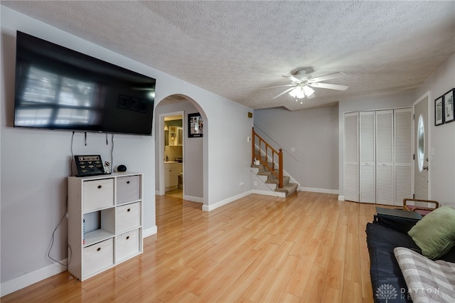 living area featuring light wood-style flooring, a textured ceiling, stairway, arched walkways, and baseboards