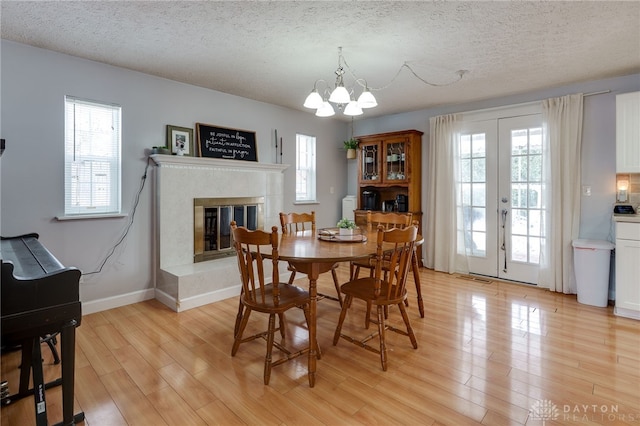 dining room with a glass covered fireplace, light wood-style flooring, french doors, and a textured ceiling