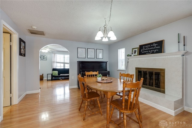 dining space with visible vents, light wood finished floors, arched walkways, a textured ceiling, and a tiled fireplace