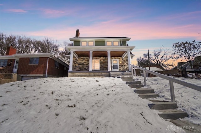 view of front of house with stone siding, covered porch, and a chimney