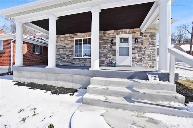 snow covered property entrance with stone siding