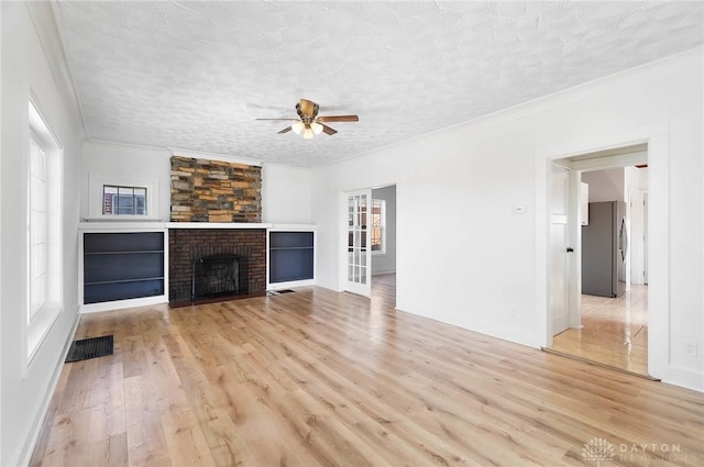 unfurnished living room with a brick fireplace, visible vents, a textured ceiling, and light wood finished floors