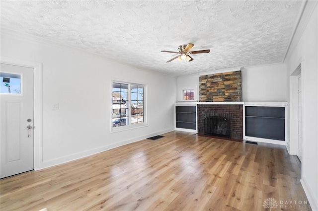 unfurnished living room with light wood-style flooring, a fireplace, visible vents, and a textured ceiling