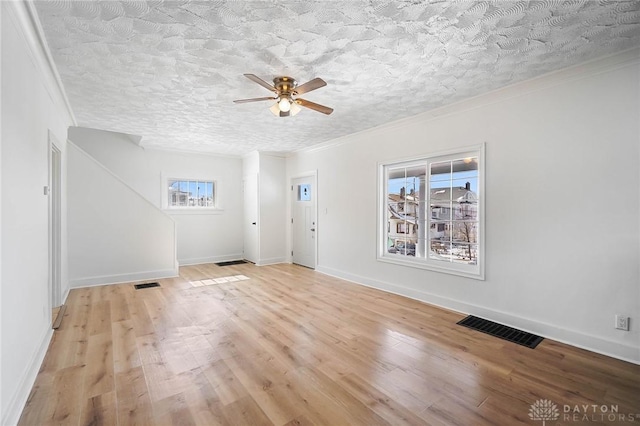 interior space with light wood-type flooring, a textured ceiling, visible vents, and crown molding