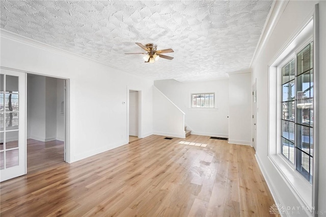 unfurnished living room featuring a textured ceiling, visible vents, light wood-style floors, stairway, and crown molding