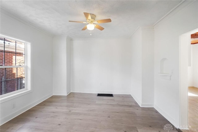 spare room featuring light wood finished floors, baseboards, visible vents, and crown molding