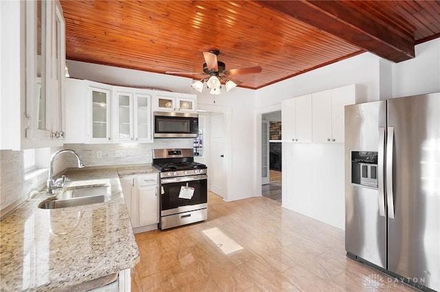 kitchen featuring light stone counters, stainless steel appliances, a sink, white cabinets, and glass insert cabinets