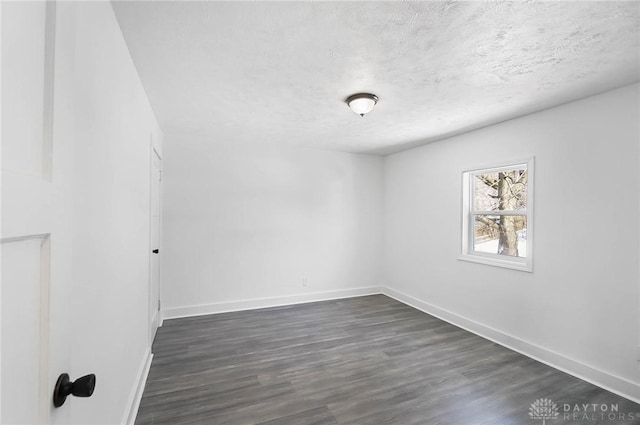 spare room featuring a textured ceiling, dark wood-style floors, and baseboards