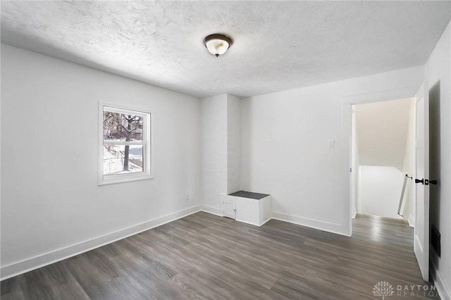 unfurnished room featuring a textured ceiling, dark wood-type flooring, and baseboards