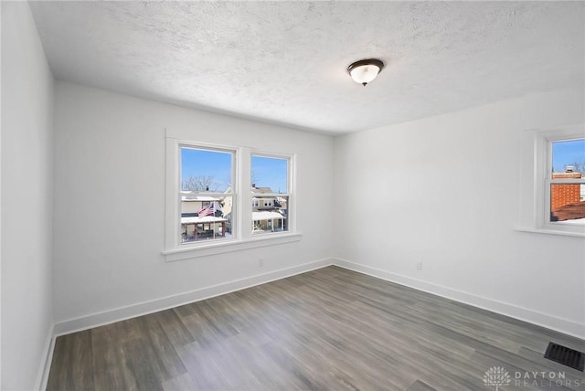 empty room with dark wood-style floors, a textured ceiling, visible vents, and baseboards