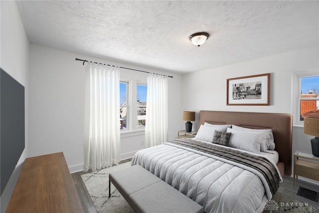 bedroom featuring light wood-style floors, baseboards, visible vents, and a textured ceiling