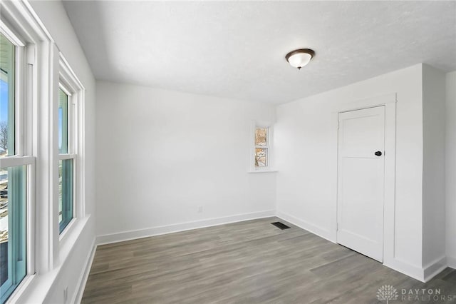 unfurnished room featuring visible vents, a textured ceiling, baseboards, and wood finished floors