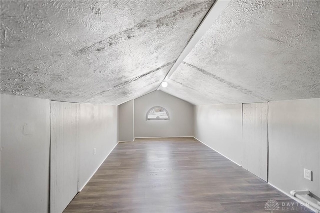 additional living space with a textured ceiling, vaulted ceiling, and wood finished floors