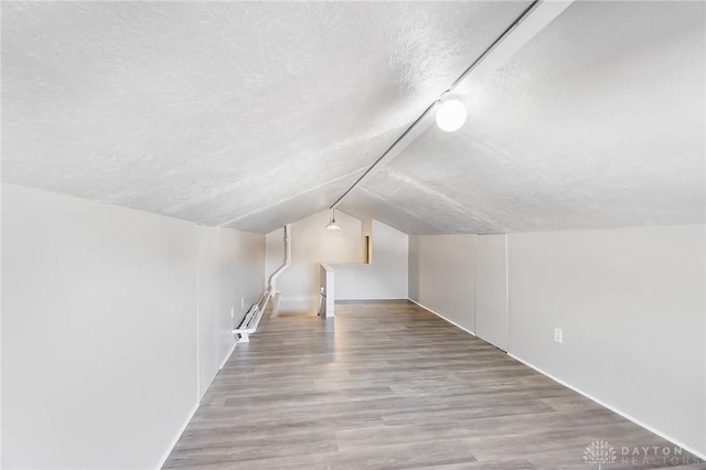 additional living space with light wood-style floors, a baseboard heating unit, vaulted ceiling, and a textured ceiling