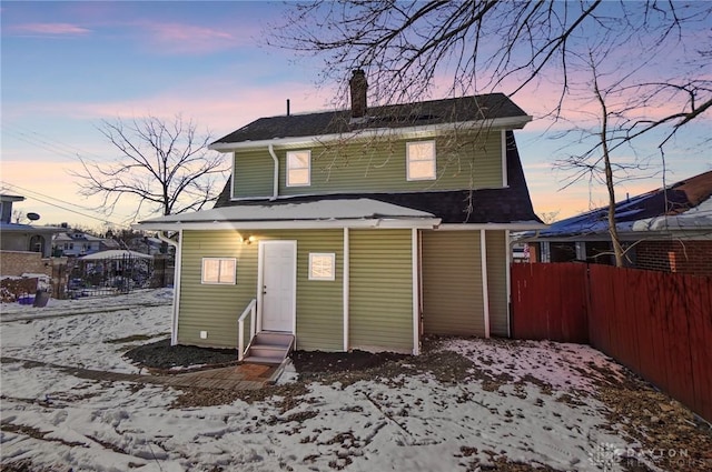 snow covered back of property with entry steps, a chimney, and fence