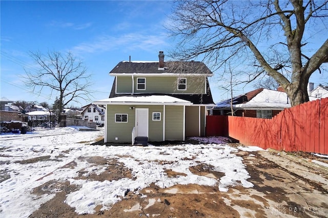 snow covered property with entry steps, a chimney, and fence