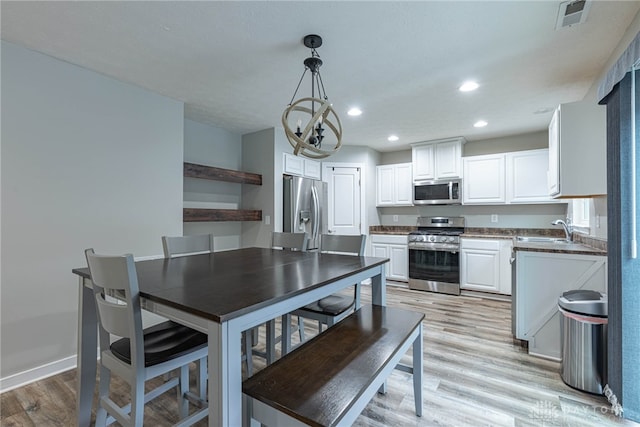 kitchen featuring decorative light fixtures, stainless steel appliances, dark countertops, white cabinetry, and a sink