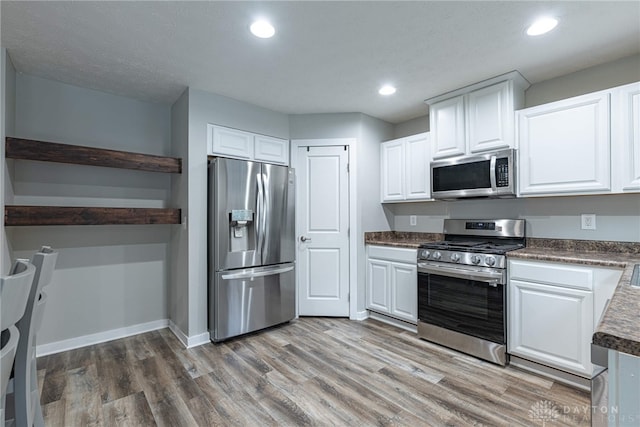 kitchen with stainless steel appliances, wood finished floors, baseboards, white cabinets, and dark countertops