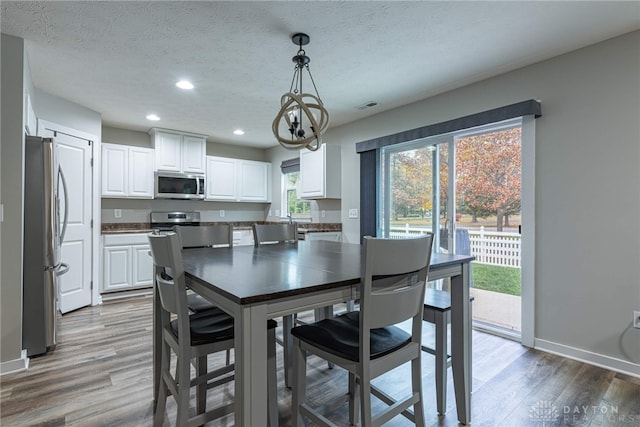 dining area with visible vents, a textured ceiling, baseboards, and wood finished floors