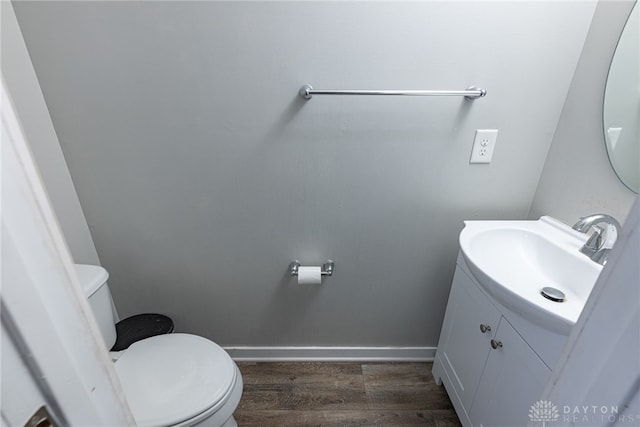 half bathroom featuring baseboards, vanity, toilet, and wood finished floors