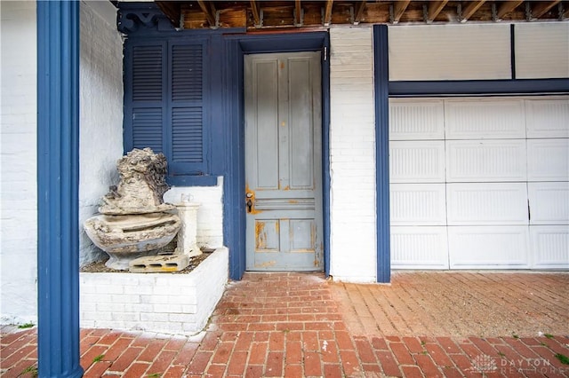 doorway to property featuring a garage and brick siding