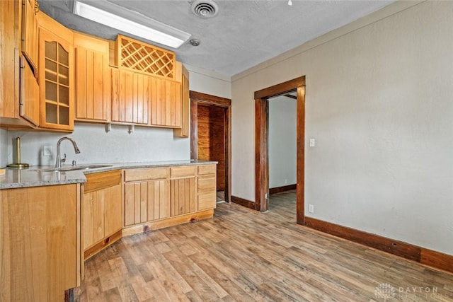 310 E Maple Ave, Miamisburg, OH 45342 - kitchen featuring a sink, light wood-type flooring, baseboards, glass insert cabinets, and light stone countertops