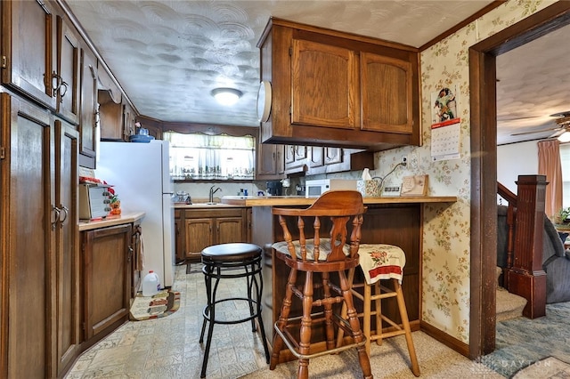 kitchen with a breakfast bar, light countertops, a sink, a peninsula, and wallpapered walls