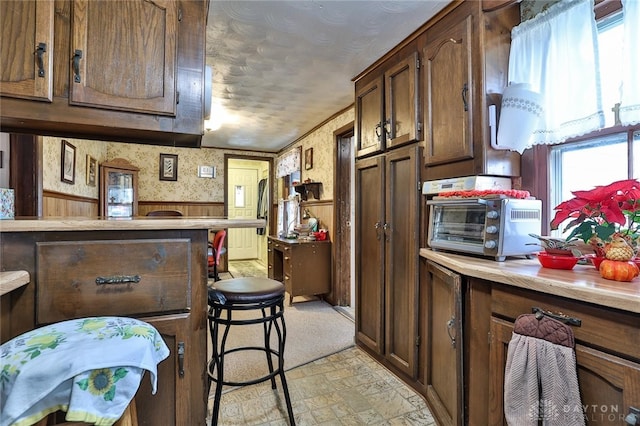 kitchen with wallpapered walls, a toaster, a wainscoted wall, a breakfast bar area, and light countertops