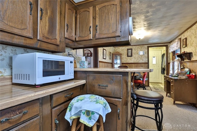 kitchen with wallpapered walls, a breakfast bar area, white microwave, and light countertops