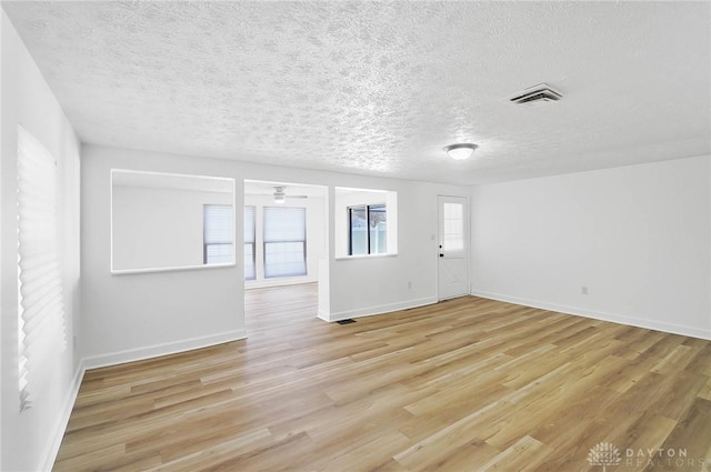 unfurnished room with light wood-style flooring, a textured ceiling, visible vents, and baseboards