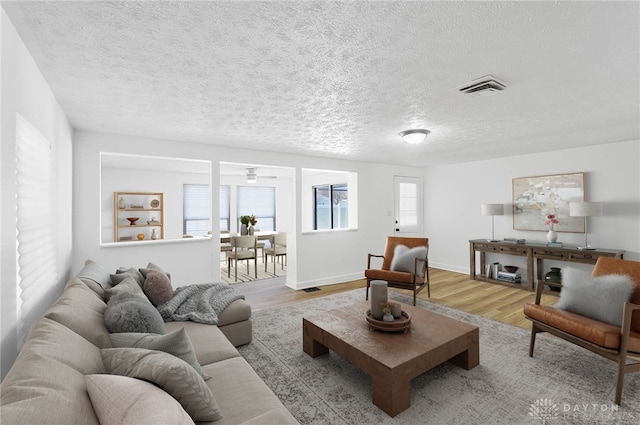 living room with light wood-style floors, baseboards, visible vents, and a textured ceiling