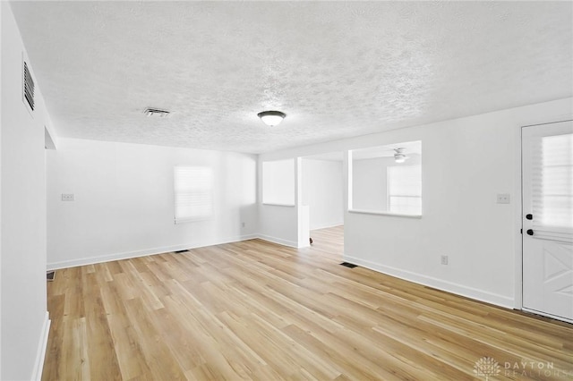 unfurnished room featuring light wood-type flooring, visible vents, a textured ceiling, and baseboards