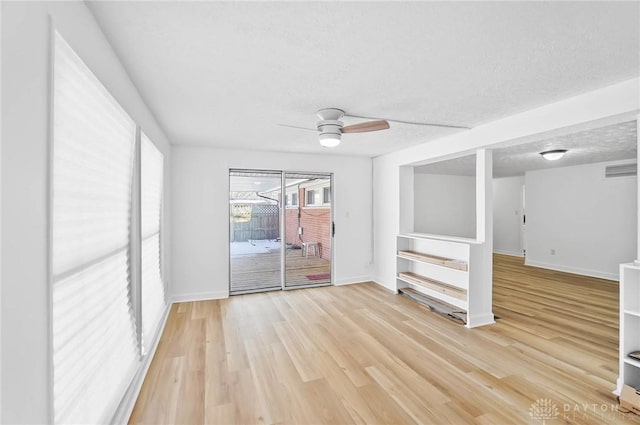 empty room featuring a textured ceiling, light wood finished floors, visible vents, and baseboards