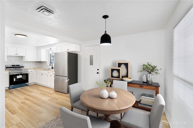 dining area with a textured ceiling, light wood finished floors, and visible vents