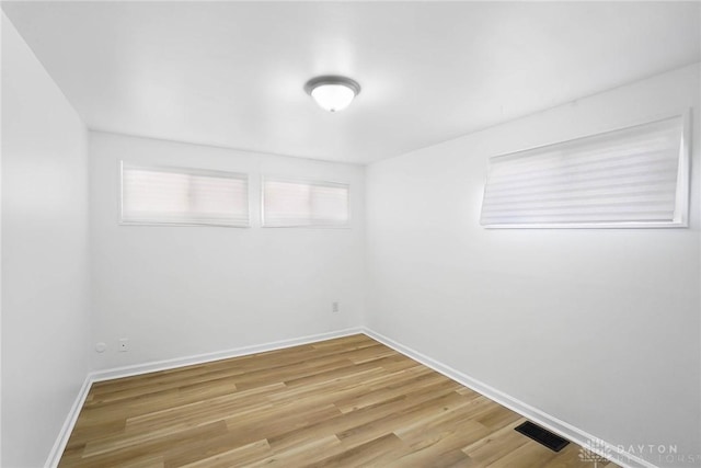 unfurnished room featuring baseboards, visible vents, and wood finished floors