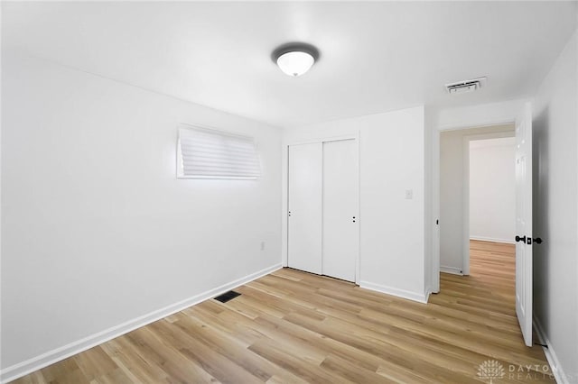 unfurnished bedroom with a closet, light wood-type flooring, visible vents, and baseboards