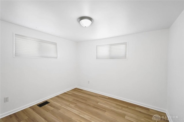 spare room with light wood-type flooring, visible vents, and baseboards