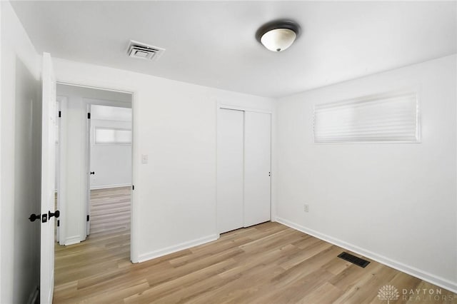 unfurnished bedroom featuring light wood-type flooring, visible vents, and a closet