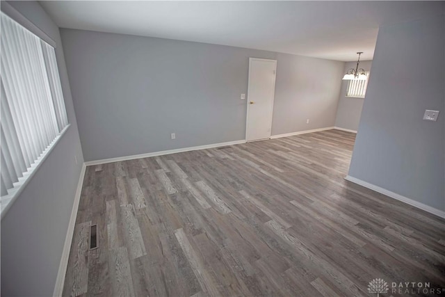 unfurnished room with an inviting chandelier, visible vents, baseboards, and wood finished floors