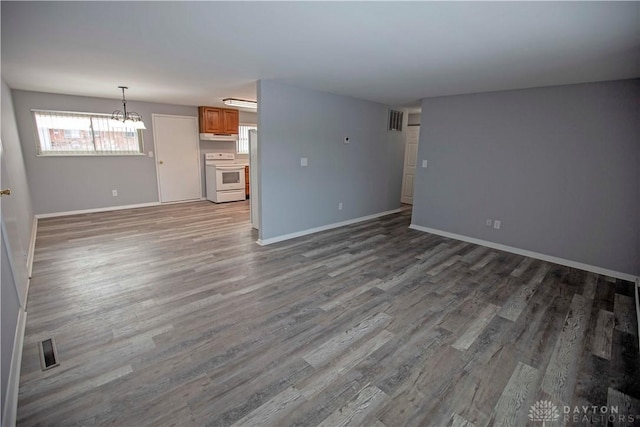 unfurnished living room featuring a chandelier, wood finished floors, visible vents, and baseboards